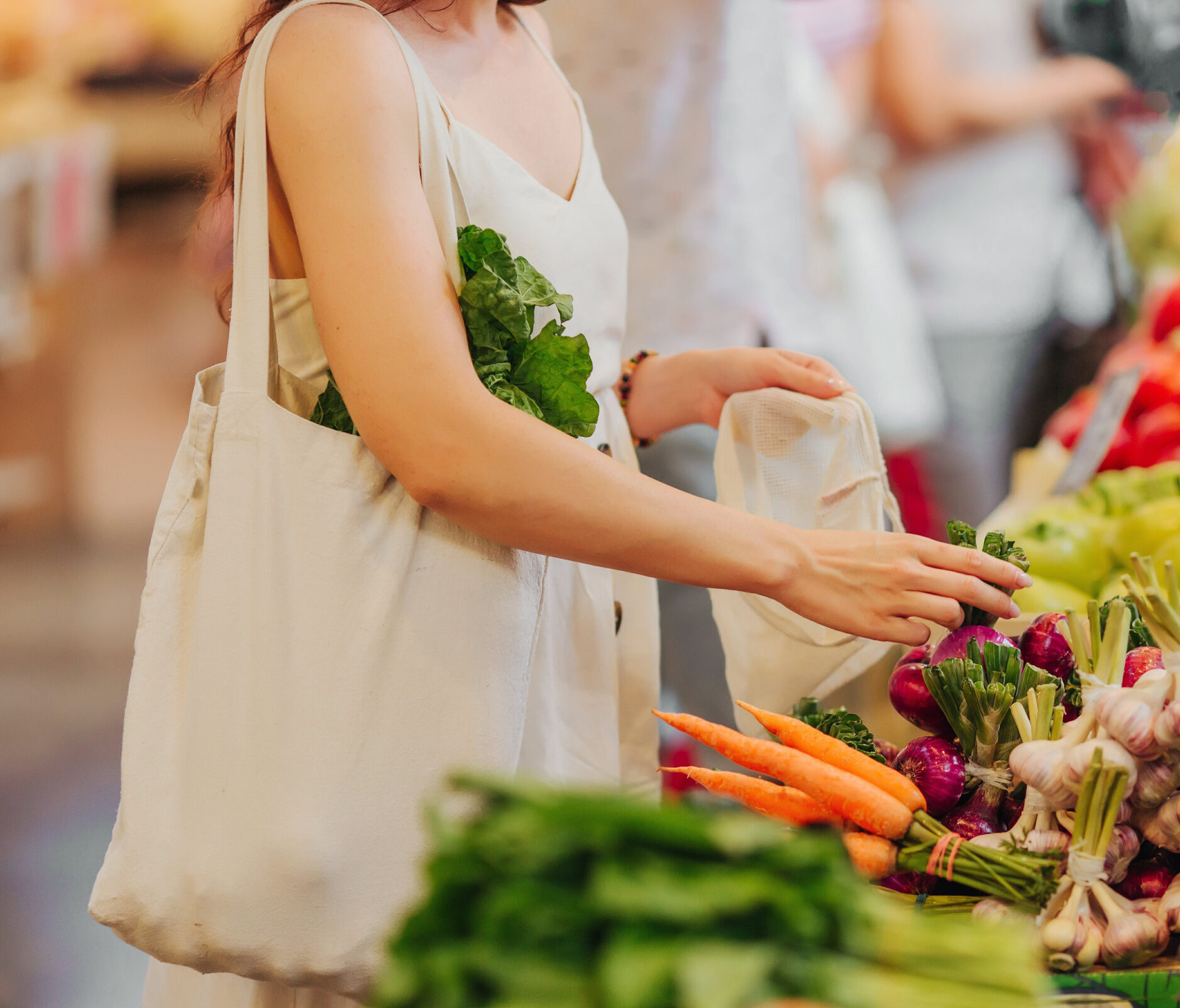 Female hands puts fruits and vegetables in cotton produce bag at food market. Reusable eco bag for shopping. Zero waste concept.