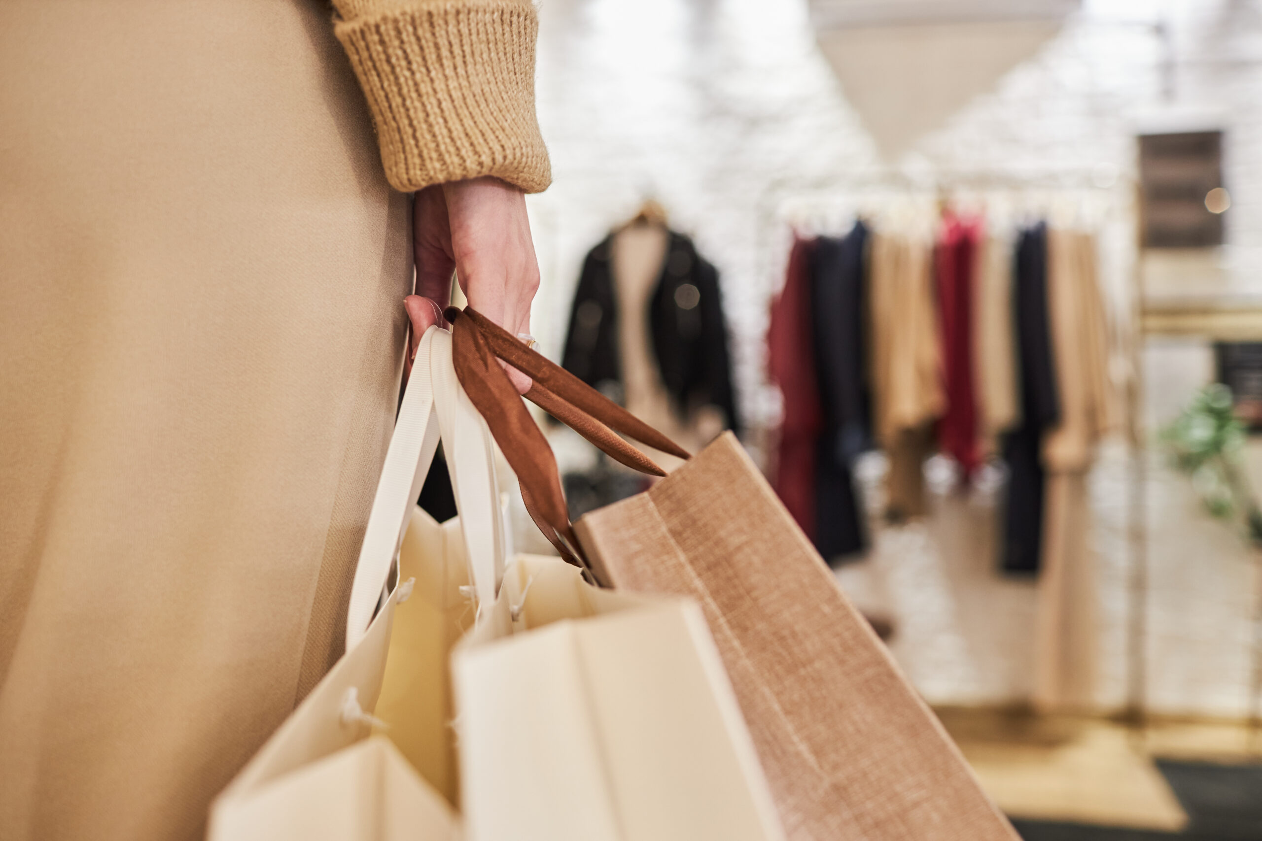 Closeup of unrecognizable young woman carrying bags with purchases in hand while shopping in clothing store, copy space