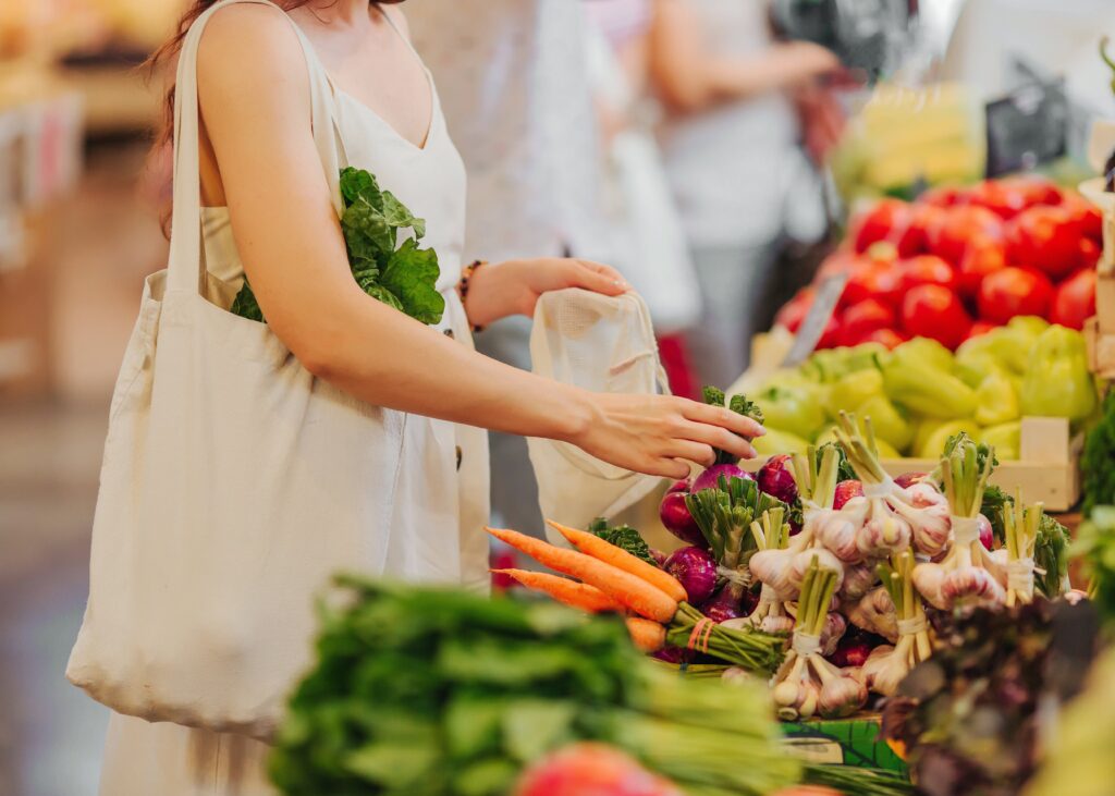 Female hands puts fruits and vegetables in cotton produce bag at food market. Reusable eco bag for shopping. Zero waste concept.