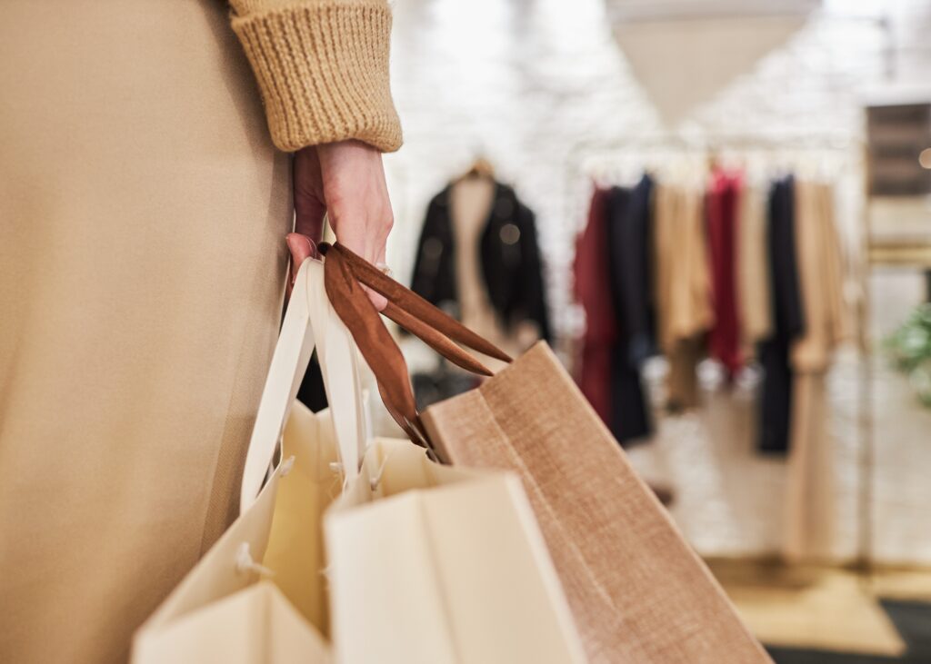 Closeup of unrecognizable young woman carrying bags with purchases in hand while shopping in clothing store, copy space