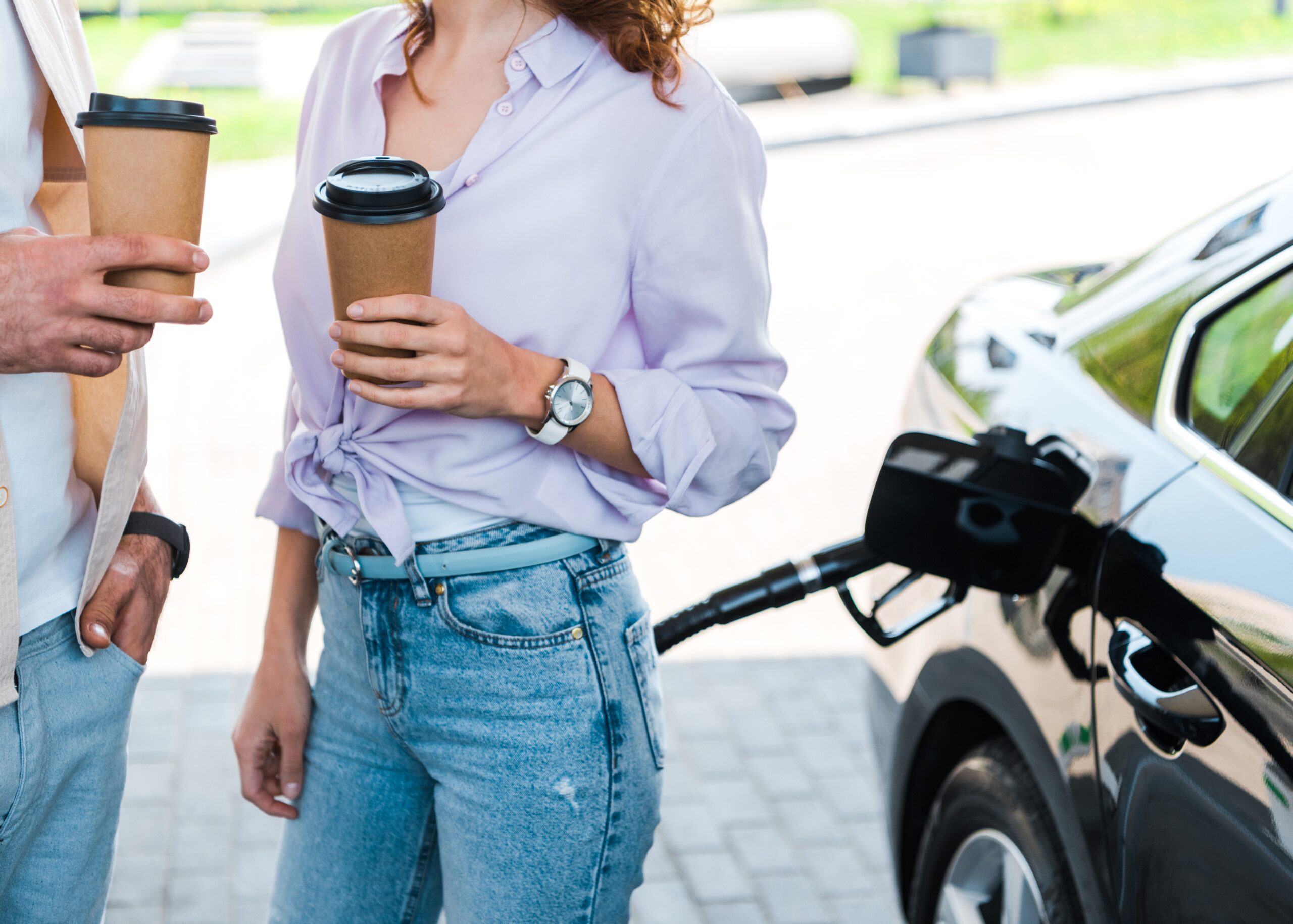 cropped view of man standing with hand in pocket near woman holding paper cup at gas station
